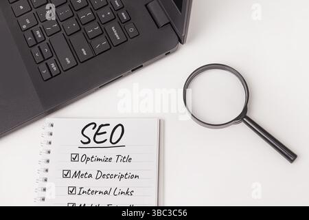 A notepad with SEO checklist, and black laptop, a magnifying glass isolated on white desk, suggesting optimization tasks and strategies for improving Stock Photo