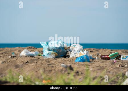 Plastic bags and bottles littered on a sandy beach by the sea Stock Photo