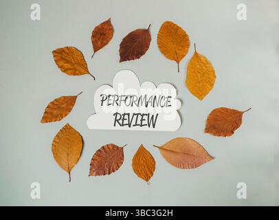 White cloud with the word performance review written on it. The cloud is surrounded by leaves. The leaves are brown and scattered around the cloud Stock Photo