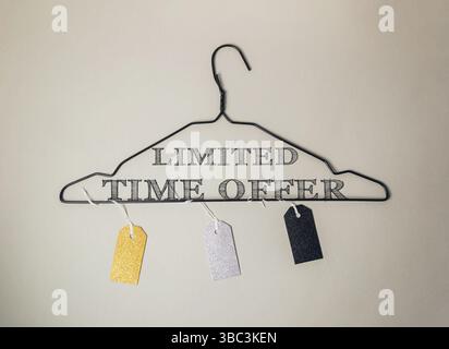 Limited time offer sign is hanging on a clothes hanger. The sign is made of metal and has a black and white font. There are three tags hanging from th Stock Photo