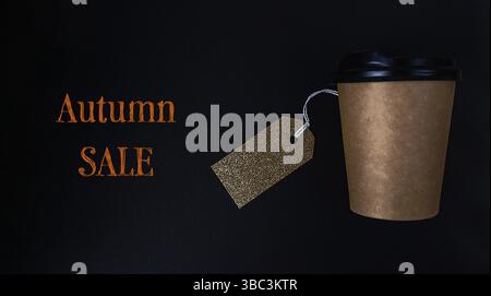 Coffee cup with a tag on it that says Autumn Sale. The tag is gold and is hanging from the cup Stock Photo