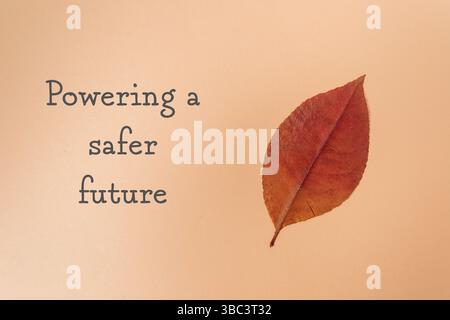 Leaf is shown on a tan background with the words powering a safer future written below it Stock Photo