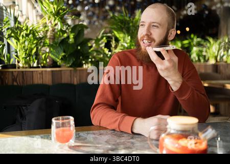 bearded man using voice assistant on mobile phone sitting at cafe. Voice Search or messages Stock Photo