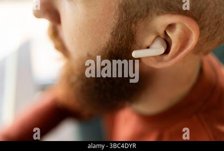 bearded businessman relaxing wearing earbud listening to music, podcast or audio book in wireless headset. Close-up, side view Stock Photo