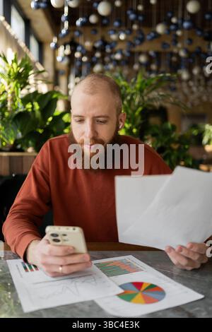 Male entrepreneur worker working remote at cafe and using phone studying documents Stock Photo