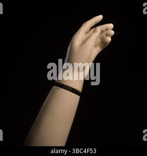 A detailed view of a mannequin hand with fingers slightly curled, creating a graceful pose against a dark background Stock Photo