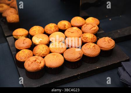 A variety of golden brown muffins arranged neatly on a dark serving tray at a breakfast buffet or catering event. Stock Photo