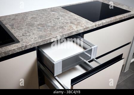 Induction cooker black glass hob or aspirating induction hob on marble stoneware countertop, with horizontal sliding pull out drawer shelves storage i Stock Photo