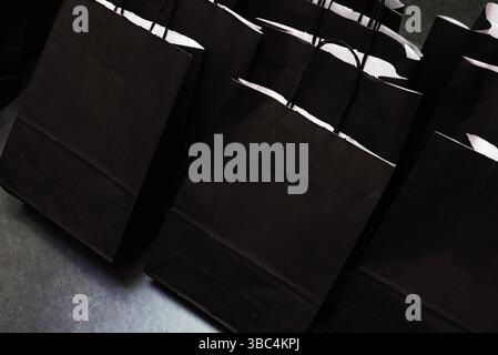 Group of elegant black paper bags with handles, arranged for guests at a corporate or promotional event as gift packages. Stock Photo
