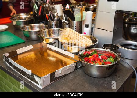 Kitchen workspace prepared for dessert making with strawberries soaking in water, ladyfingers, mixing bowls, and baking tray. Stock Photo