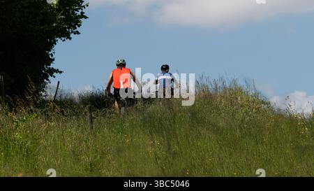 Cyclists Exploring a Scenic Trail Through Meadow Grass and Sunny Blue Sky Stock Photo