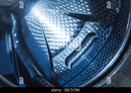 Detailed view showing the textured and reflective stainless steel interior of a washing machine drum, highlighting its design and functionality. Abstr Stock Photo
