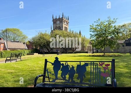 All Saints Parish Church of Wigan and gardens. Back of bench remembering sacrifice of war with poppies and soldiers on battlefield in cutout’s Stock Photo