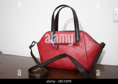 A red colored handbag is on the wooden surface with a blue pen. Stock Photo
