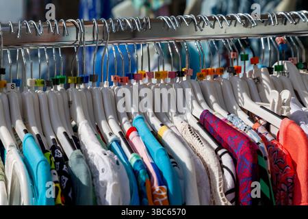 Close-up on a clothing rack filled with a variety of colorful garments on white plastic hangers. Stock Photo