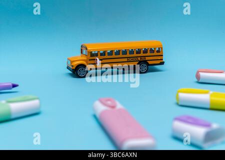 Yellow school bus placed on blue background, surrounded by colored markers. The composition is playful and educational, suitable for themes related to Stock Photo