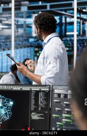 Data center admin uses AI visualization technology on tablet to oversee automated repetitive tasks. Server farm IT professional modifying infrastructure rigs systems based on data analytics graphs Stock Photo