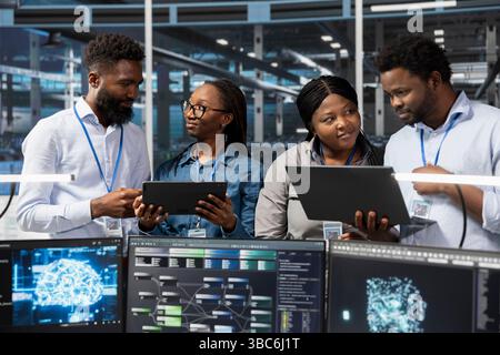 Teamworking server room colleagues use artificial intelligence to perform computing tasks. Data center engineering team doing brainstorming, working together, using AI for machine learning workloads Stock Photo