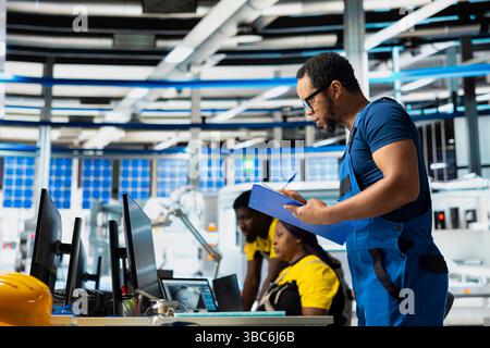 Supervisor testing solar power in renewable energy facility on clipboard, focusing on software troubleshooting and performance metrics. Eco friendly quality control on operations. Stock Photo