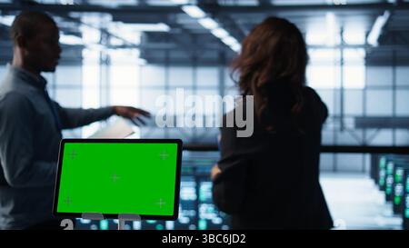 Close up of chroma key tablet next to server room data scientists conducting security audits, preventing bugs. Green screen device and man working with colleague in data center, camera B Stock Photo
