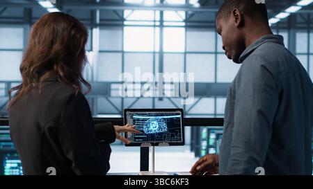 Data center team reviewing paperwork in server room, analyzing system reports using AI on tablet. Artificial intelligence server room admins looking over financial documents, camera A Stock Photo