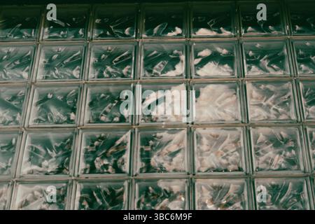 Textured glass block wall in a repeating square pattern, creating an artistic abstract composition. A textured glass block wall in a bathroom interior Stock Photo