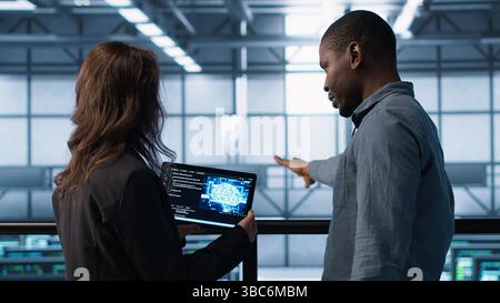 Data center technicians deploying AI driven management tools using tablet. Server farm coworkers inspecting server clusters, updating network topologies using artificial intelligence, camera A Stock Photo