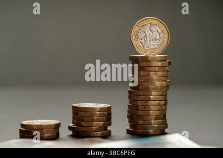 Three increasing stacks of one pound coins arranged in ascending order with blurred banknotes in foreground, illustrating income growth and financial Stock Photo