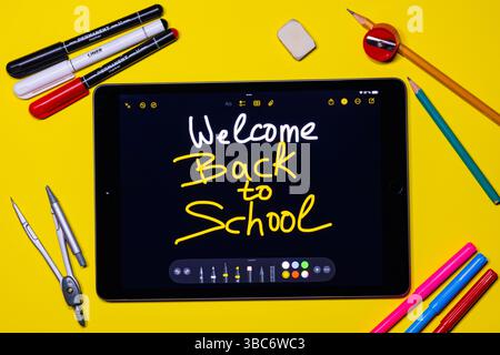 Top view of black tablet with handwritten 'welcome back to school', school and office supplies are laying around on yellow background Stock Photo