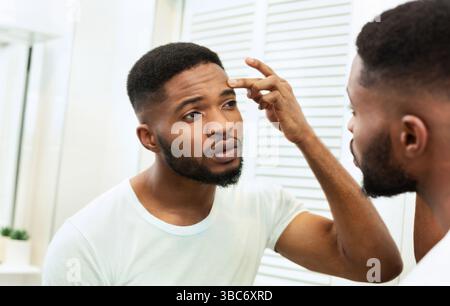 Young worried african man checking his wrinkles Stock Photo