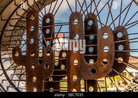Rusty-brown, artistically shaped metal cacti adorn a wall in the El Jardín de Cactus cactus garden on Lanzarote, where around 4,500 species of cacti from five continents are on display. It was designed by César Manrique and is laid out in a former landfill site as a terraced amphitheatre with lava stone walls. Avenida Garafía, Guatiza, Canarias, Spain Stock Photo