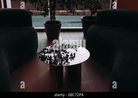 Stylish indoor space featuring two armchairs, a round table, indoor plants near a window. A modern interior setting with armchairs, a reflective table Stock Photo