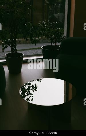Stylish indoor space featuring two armchairs, a round table, indoor plants near a window. A modern interior setting with armchairs, a reflective table Stock Photo
