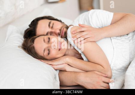 Loving young couple having cozy morning, cuddling together in their sleep on bed Stock Photo