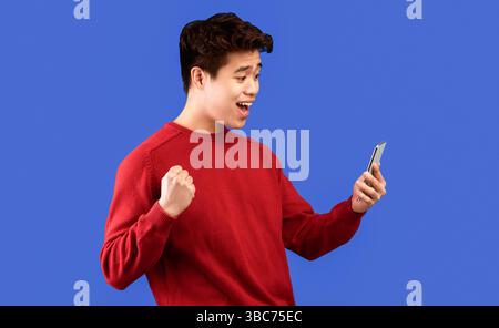 Excited asian man using mobile phone, celebrating online win Stock Photo