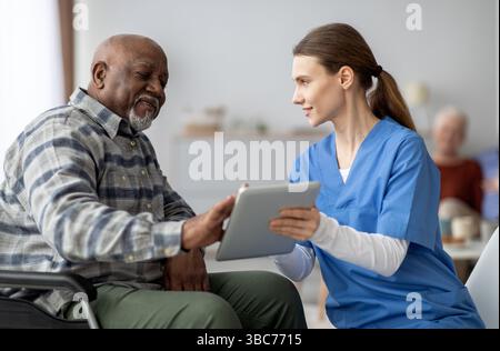 Friendly nurse helping black senior man using digital tablet Stock Photo