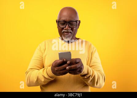 Happy senior black man using smartphone, writing message, chatting with friend, surfing internet, watching movie online Stock Photo