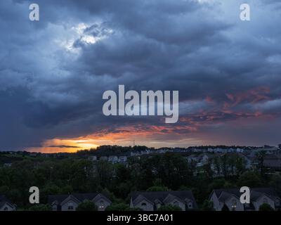 A vivid sunset contrasts with dark storm clouds and visible rain over houses in a suburban neighborhood near Pittsburgh, PA. Stock Photo