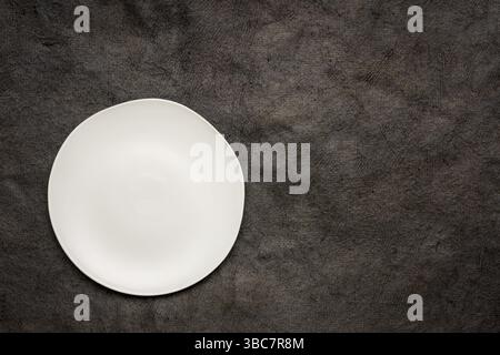 White ceramic plate with an irregular edge on a black handmade Huun Mayan paper with a copy space Stock Photo