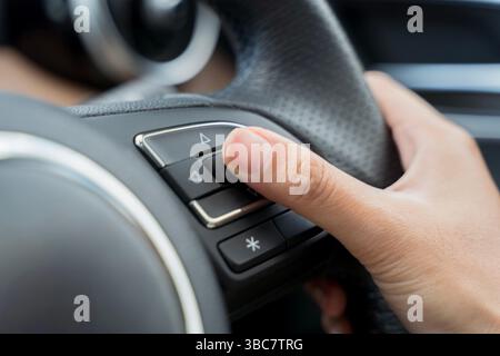 Driver’s hand pressing button on steering wheel in modern car, used for controlling vehicle functions like audio or cruise control. Concept of smart d Stock Photo