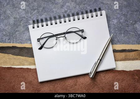 Blank spiral art sketchbook with a pen and reading glasses, reading glasses against abstract paper landscape in earth tones Stock Photo