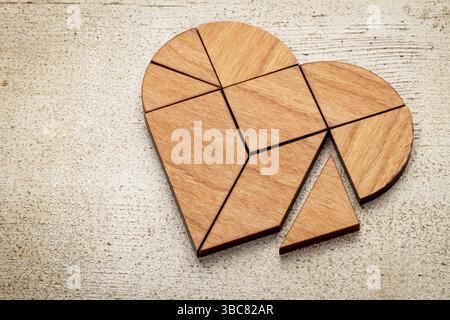 Heart version of tangram, a traditional Chinese Puzzle Game made of different wood parts to build abstract figures from them, on white painted barn wo Stock Photo