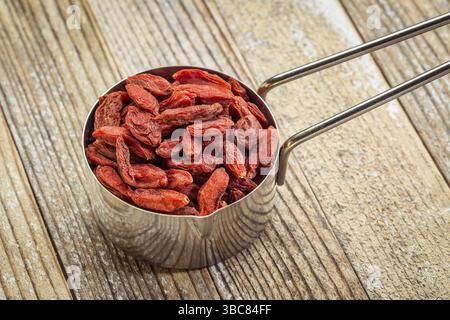 Dried goji berries in a metal measuring scoop against grunge wood background Stock Photo