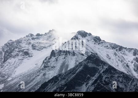 Snow-covered rugged mountain peak under cloudy sky Stock Photo