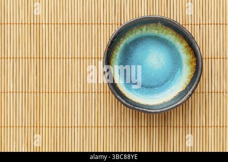 Small empty ceramic bowl (sauce dish) with blue enamel on bamboo placemat Stock Photo