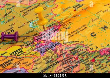 A topographical map displays Kyrgyzstan and neighboring countries, featuring a yellow and purple push pin to mark locations for geographical reference Stock Photo