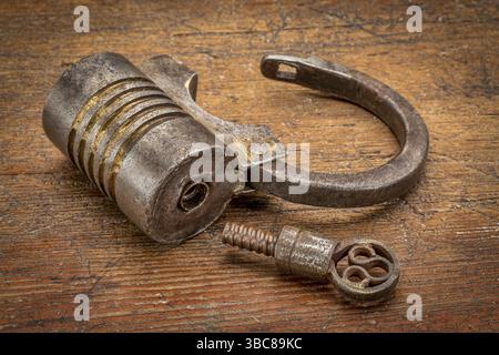 Vintage round shape hand crafted screw type iron padlock (unlocked) with a key on rustic wood Stock Photo