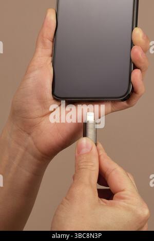 woman hand plugging charger cord into smartphone to charge battery on beige background, Wired charging close-up Stock Photo