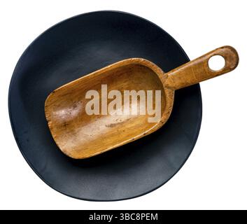 Empty rustic wooden scoop on a black ceramic plate with an irregular edge isolated on white Stock Photo