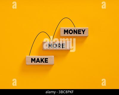 Wooden blocks form an increasing graph with the words make more money on a yellow background, representing the concept of earning and profit. Stock Photo